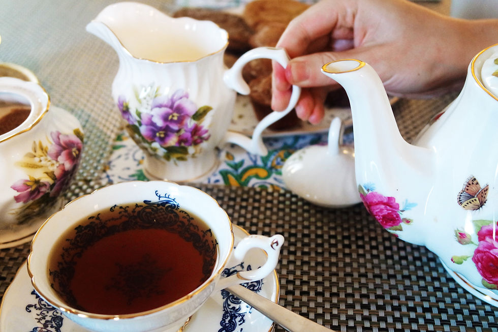 Blue and white pattern tea cup with tea in the foreground and a hand reaching for the creamer, white with purple flowers.