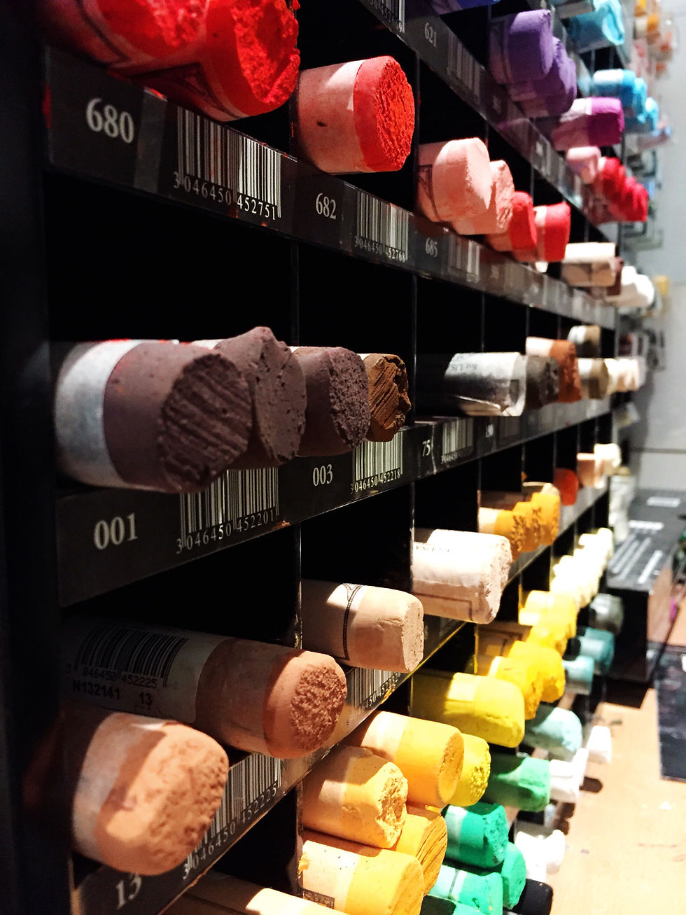 Close of up shot of large pastel sticks sitting in a set of black shelves, sorted by color.