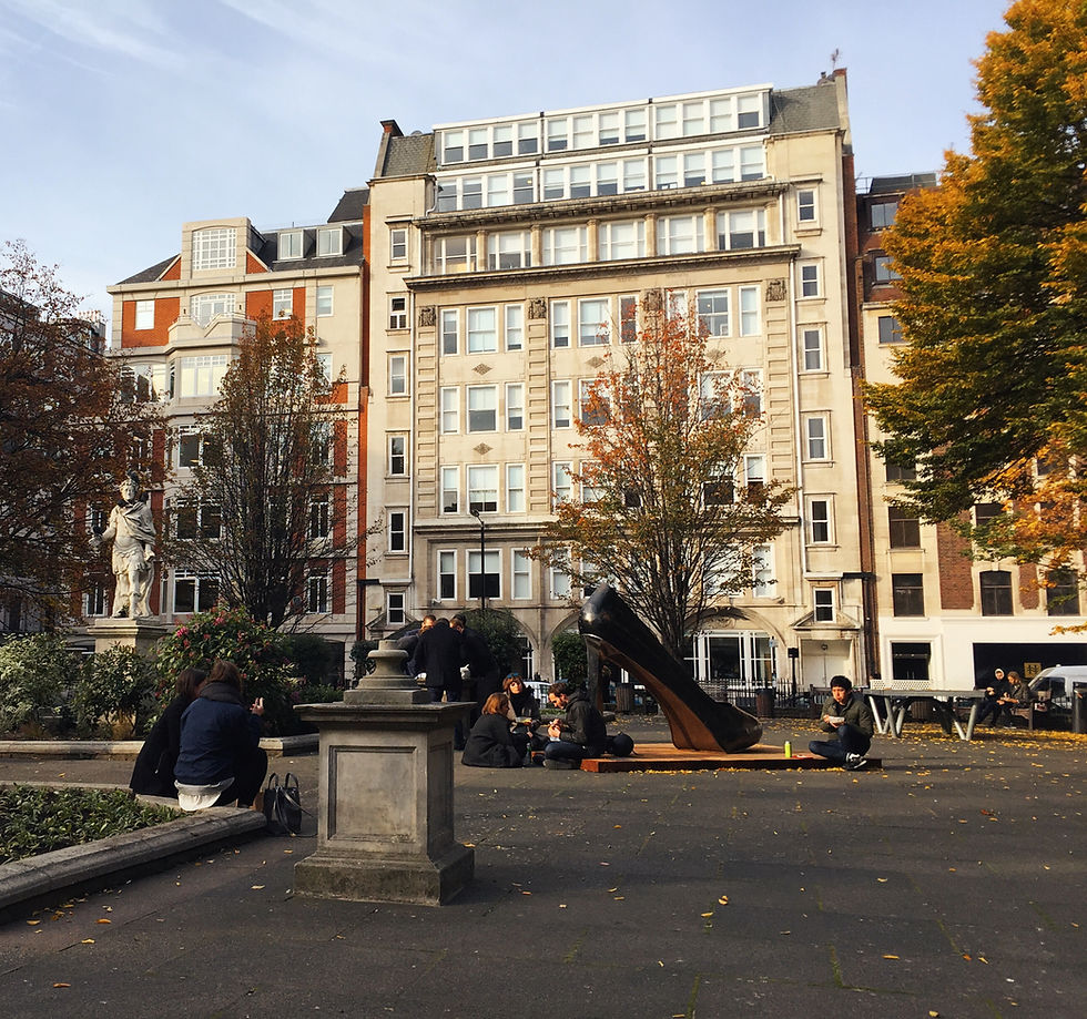 Golden Square in London, in the Fall. People sitting and eating lunch. Gold tipped trees. A statue of a high heeled shoe. And a view of a Georgian style building.