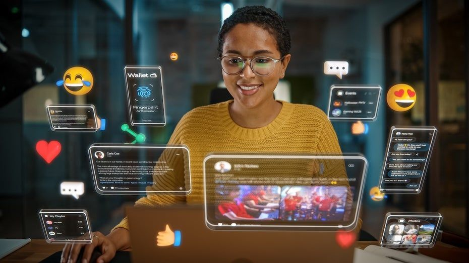Smiling person in a yellow sweater uses a laptop, surrounded by floating social media icons and notifications. Dimly lit office setting.