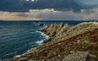 Dramatic view of the Pointe du Raz cliffs in Brittany, with waves crashing against the rocks under a stormy sky