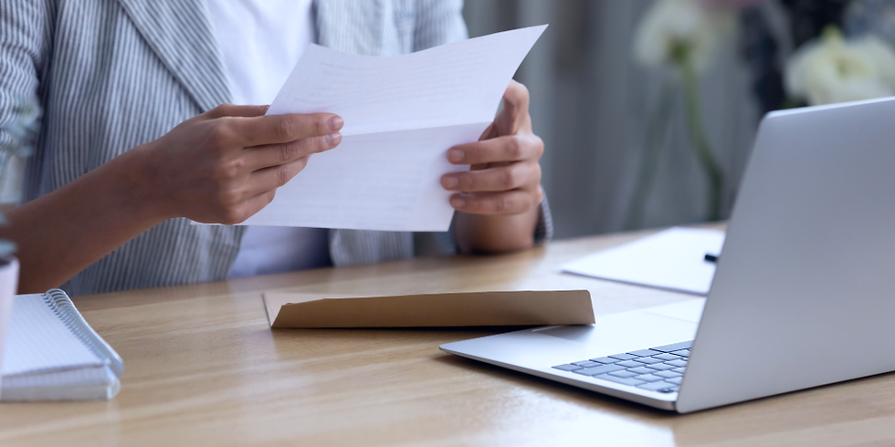 Person at a desk reading a letter next to a laptop