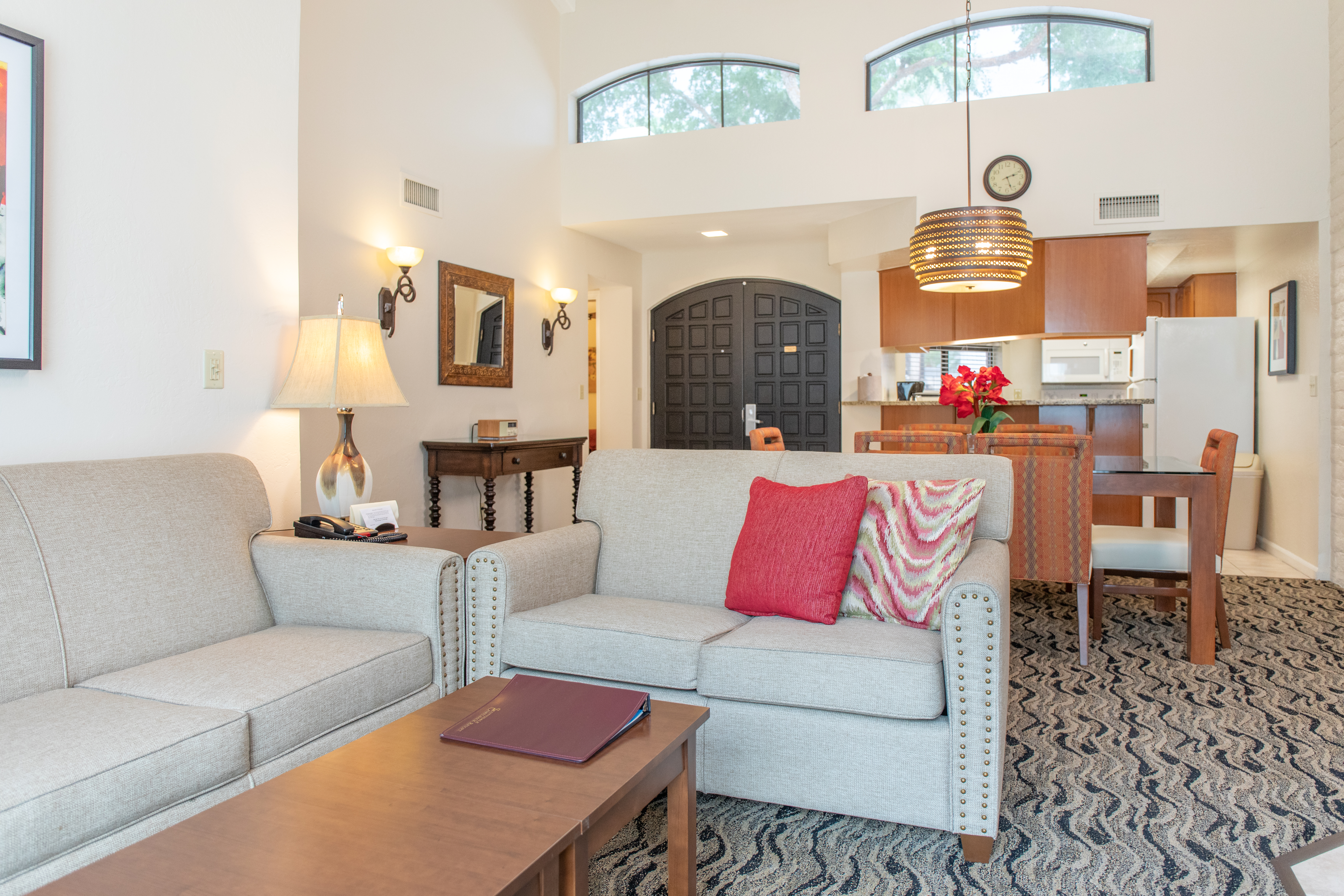 Light grey sofas with red and pink cushions, arched windows and a wooden kitchen fill a living room.