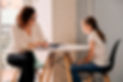 Sunstone Psychology Group smiling Psychologist with pen, paper and clipboard sits at mid-century modern table with smiling caucasian girl ready to answer questions