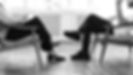 Counseling services in person with woman on left with legs crossed wearing black heels and writing on notebook and man on right wearing boots and legs crossed with elbow on arm of chair