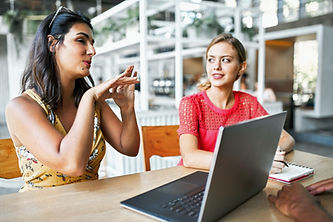 Clinical Supervision two women sit at wooden table talking about client with laptop | Psychology Clinical Supervision | Therapist Supervision