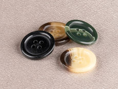 Black button, marbled brown buttons and green button with 4 holes each on khaki fabric
