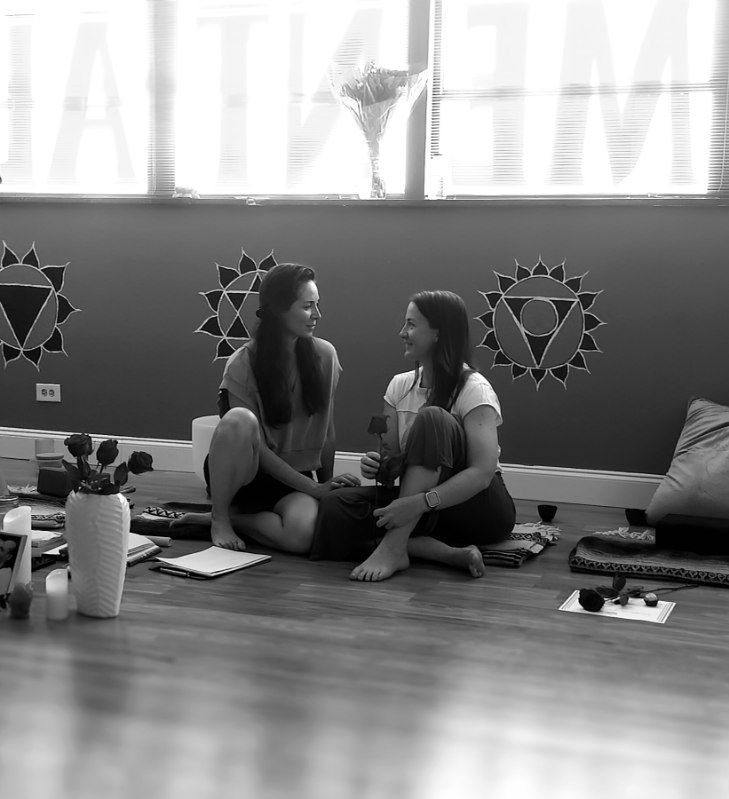 two women sitting on yoga mats and smiling