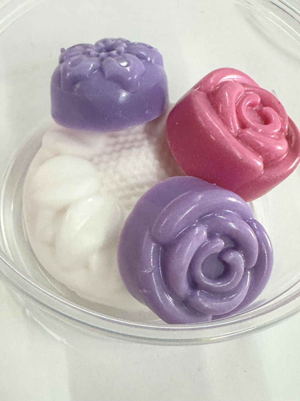 Rose-shaped soaps in purple, pink, and white colors on a clear tray.