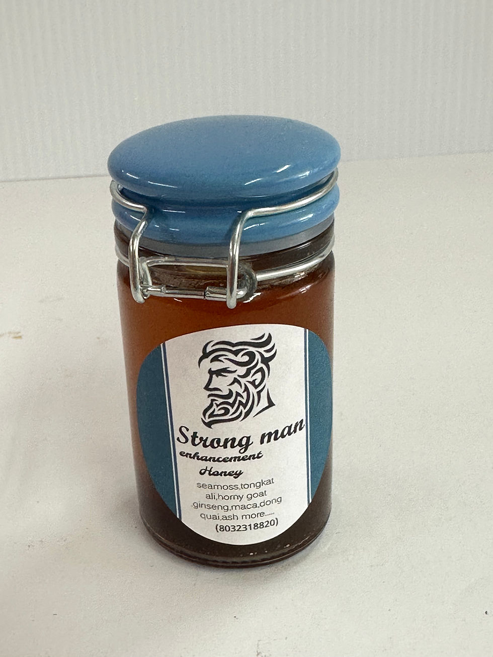 Jar of Strong Man honey with paper label, blue lid, and honey inside.