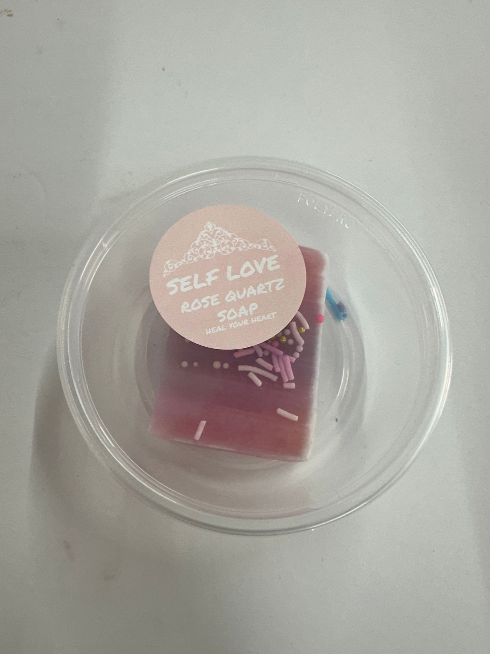 Pink soap in a clear container with the words SELF LOVE Rose Quartz Soap.