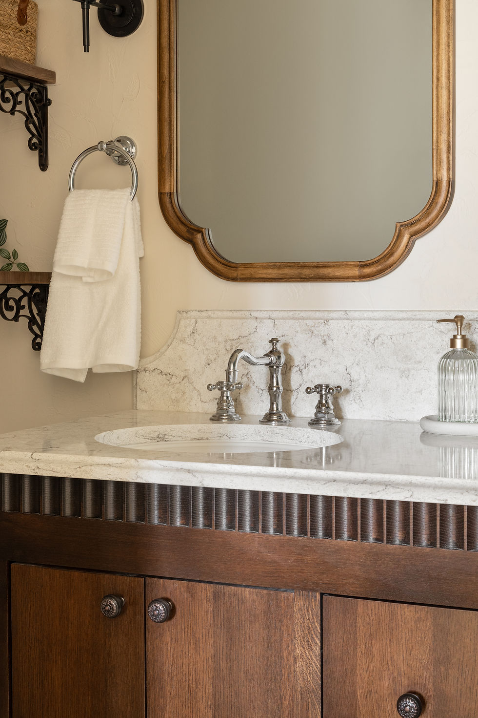 Bathroom vanity with white marble countertop, chrome faucet, wooden mirror, towel on ring, and decorative shelf. Calm, elegant setting.