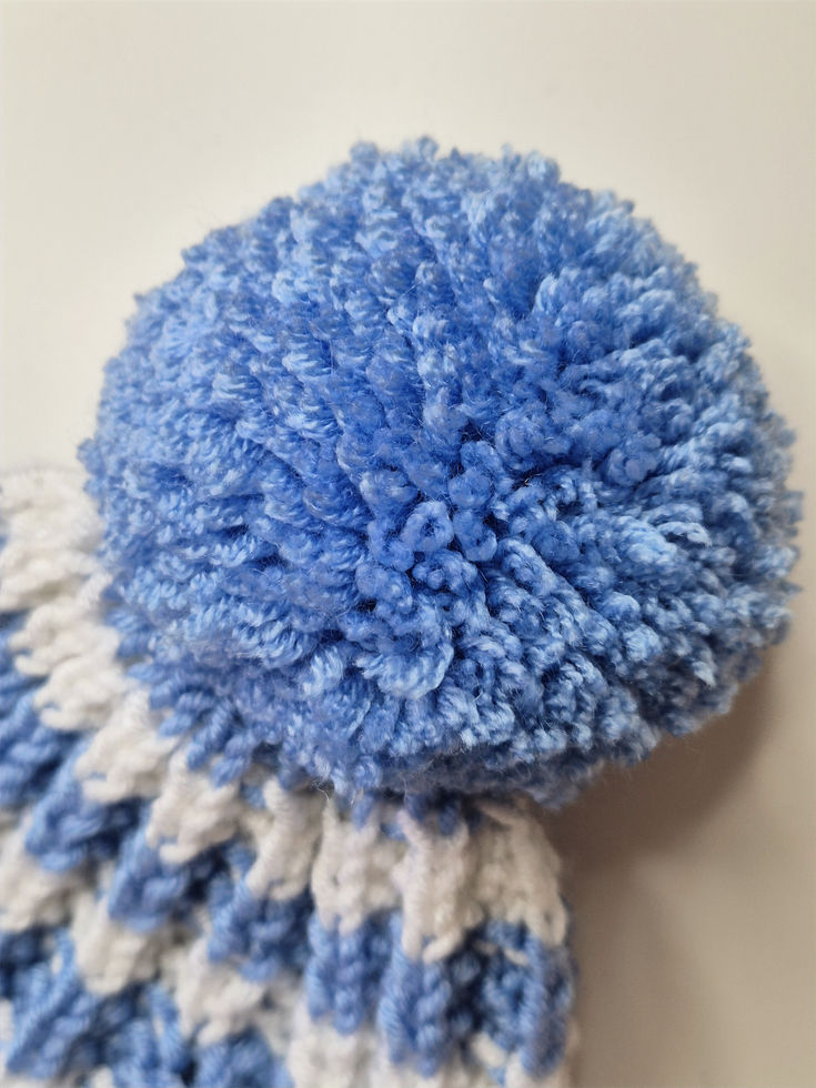 Close-up of a fluffy, light blue pompom on a striped knitted beanie.