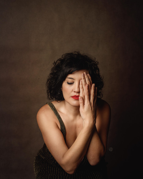 Mujer morena con cabello corto y rizado y labios rojos, con mano cubriendo la mitad de su rostro