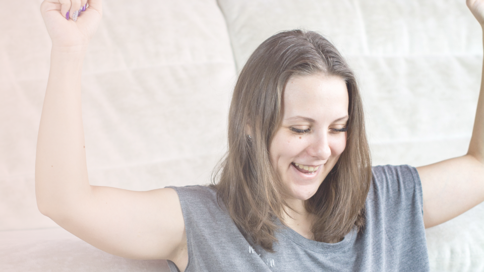 A white woman is raising her hands in triumph while smiling and staring down.