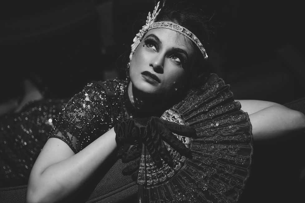 Southeast Asian female in glamorous clothing from 1920s. Holding a fan in right hand. Black and white photo
