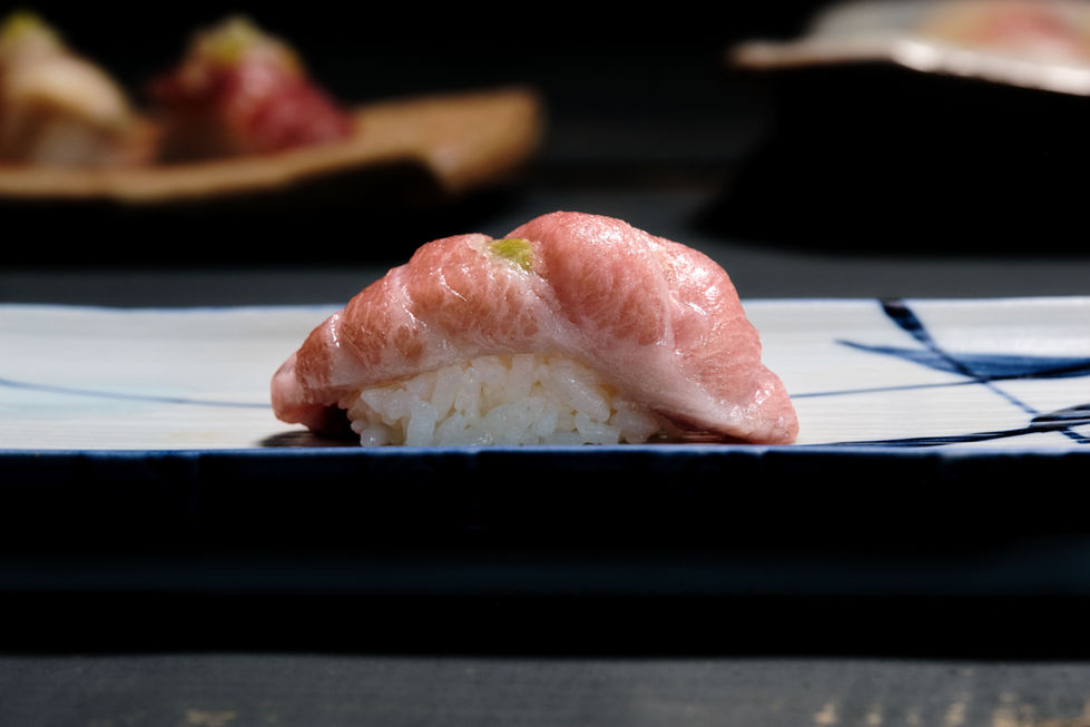 Side view of fatty tuna nigiri sushi on blue and white sushi plate.