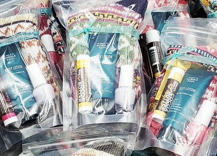 Multiple gift bags containing body lotion, chapstick, nail polish, and a of socks.