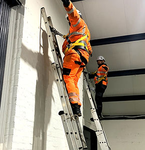 Technicians wearing PPE climbing ladders and using fall-arrest harnesses during TETRA telecoms installation and working at heights safety training.