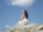 woman sitting on a rock looking up at the sky. Representing the angel number 1111 and the message to believe and have unrestricted faith.