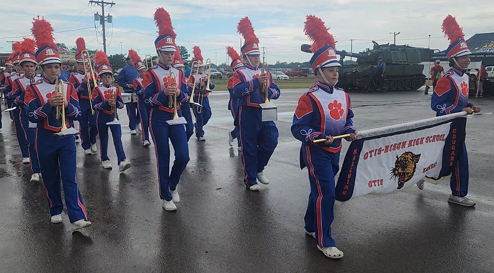 Students marching, holding their instruments. The banner is prominently held at the front.