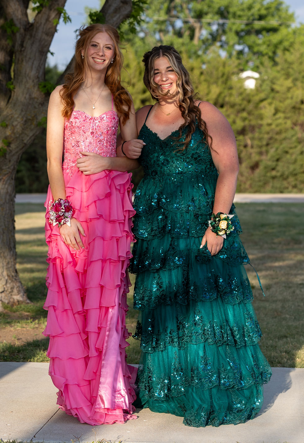 Junior Lily poses in a bright pink, layered floor-length gown. Her escort is Freshman Rowyn wearing a turquoise, layered floor-length gown with embellishments. Lilly wears a red corsage and Rowyn wears a white corsage.