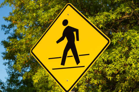 Yellow pedestrian crossing sign with trees and blue skies in the background.
