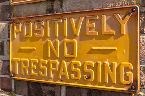 Yellow Positively No Trespassing sign on brick wall.