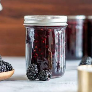Jar of homemade blackberry jam with fresh berries on a counter.