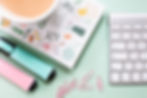 A computer keyboard on a green background alongside a book, paperclips, pens and a cup of tea, to show how email marketing is a great way to promote your business.
