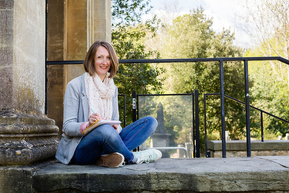 A woman sitting cross legged on the steps of a Victorian church with a notepad and fountain pen on her knee