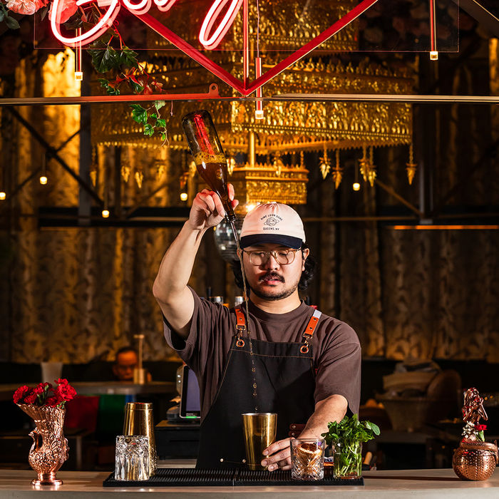 Bartender pouring a drink under a pink “Hello Gorgeous” neon sign, bar photography