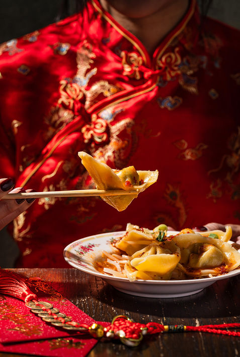 Chopsticks lifting a dumpling over a plated dish on a red table, restaurant food photography