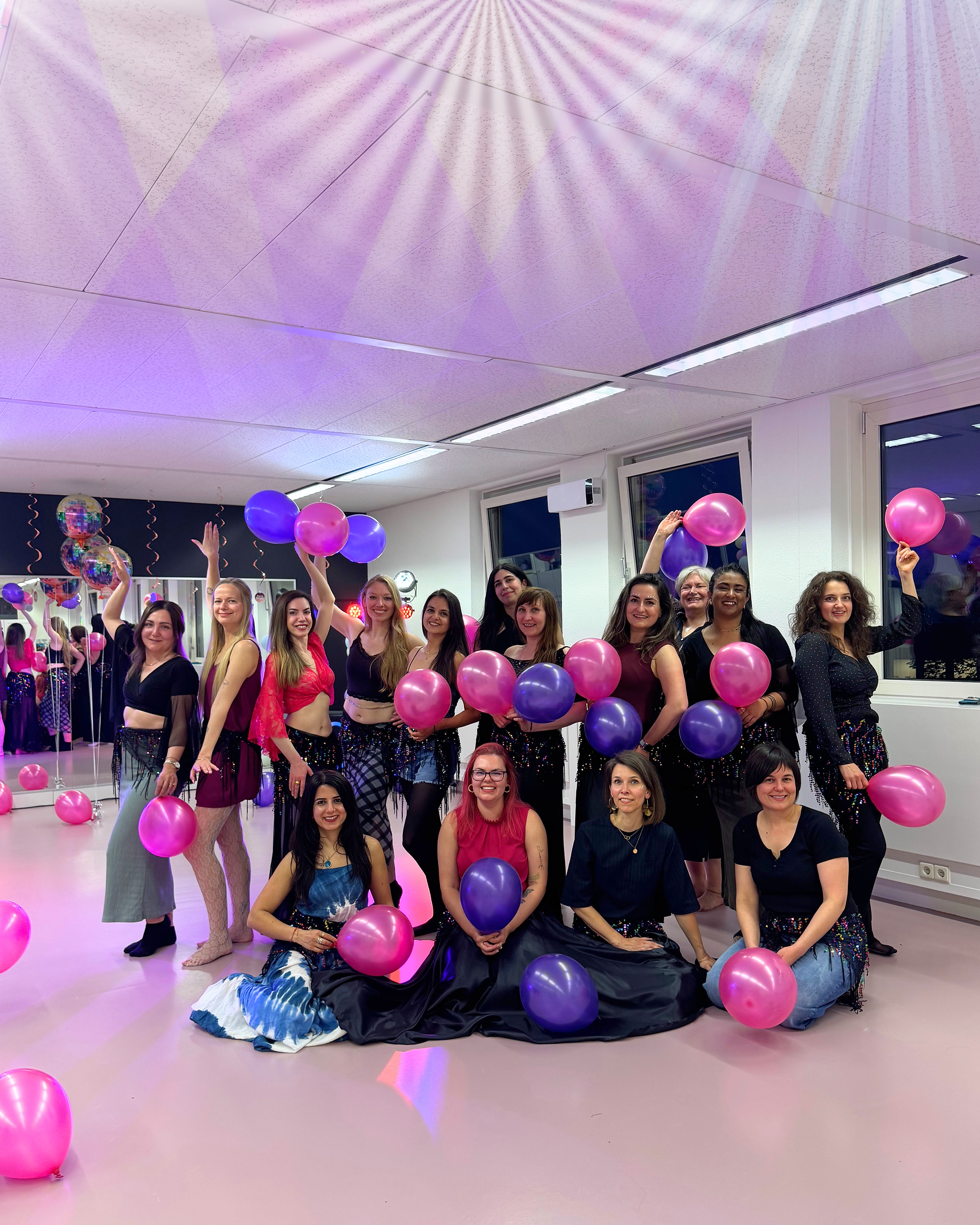 Grote groep buikdansstudenten poseert met ballonnen in de studio van Joy Dance Lab
