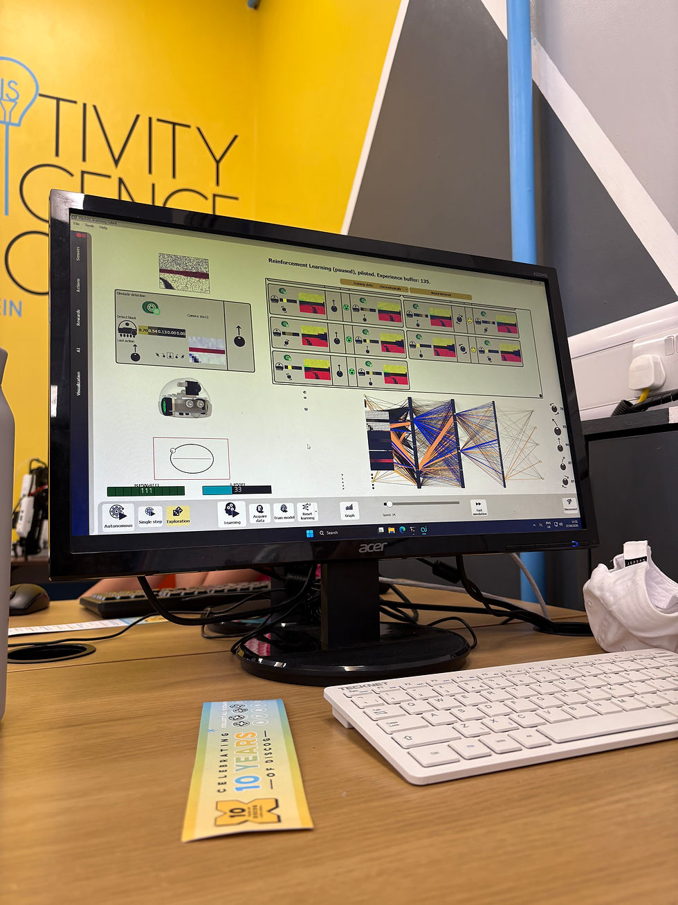 AlphAI training screen showing reward and level progress, with a DiscoG 10th anniversary bookmark on the desk