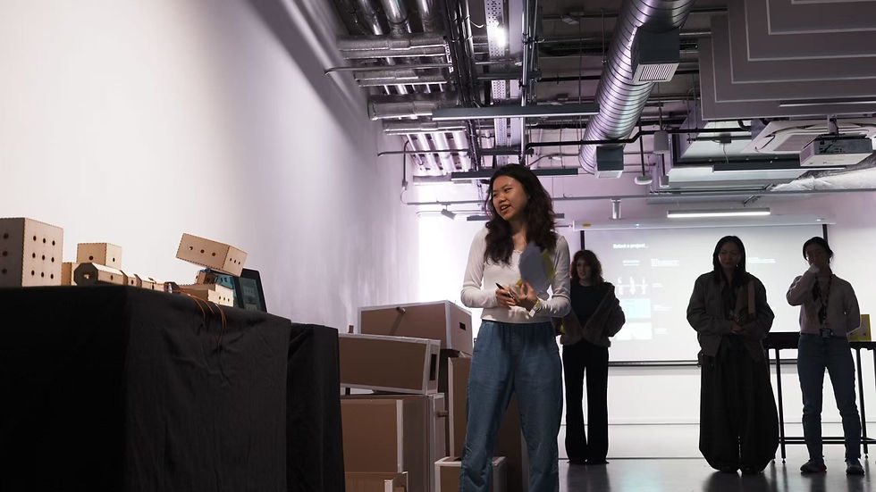 Chang Shu presenting her human-robot interaction masters project at her degree show with wooden robot prototypes displayed beside her