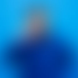 Homme barbu en pull bleu, œil grossi à la loupe, clin d’œil et bouche ouverte sur fond bleu.