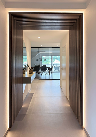 Moderner Flur mit großem, dunklem Holz-Lamellenrahmen und indirekter LED-Beleuchtung; Blick durch den Gang auf eine Glaswand und ein Esszimmer mit Tisch und Stühlen.