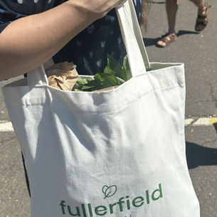 A shopper at a farmers market carrying a Fullerfield tote bag with fresh greens