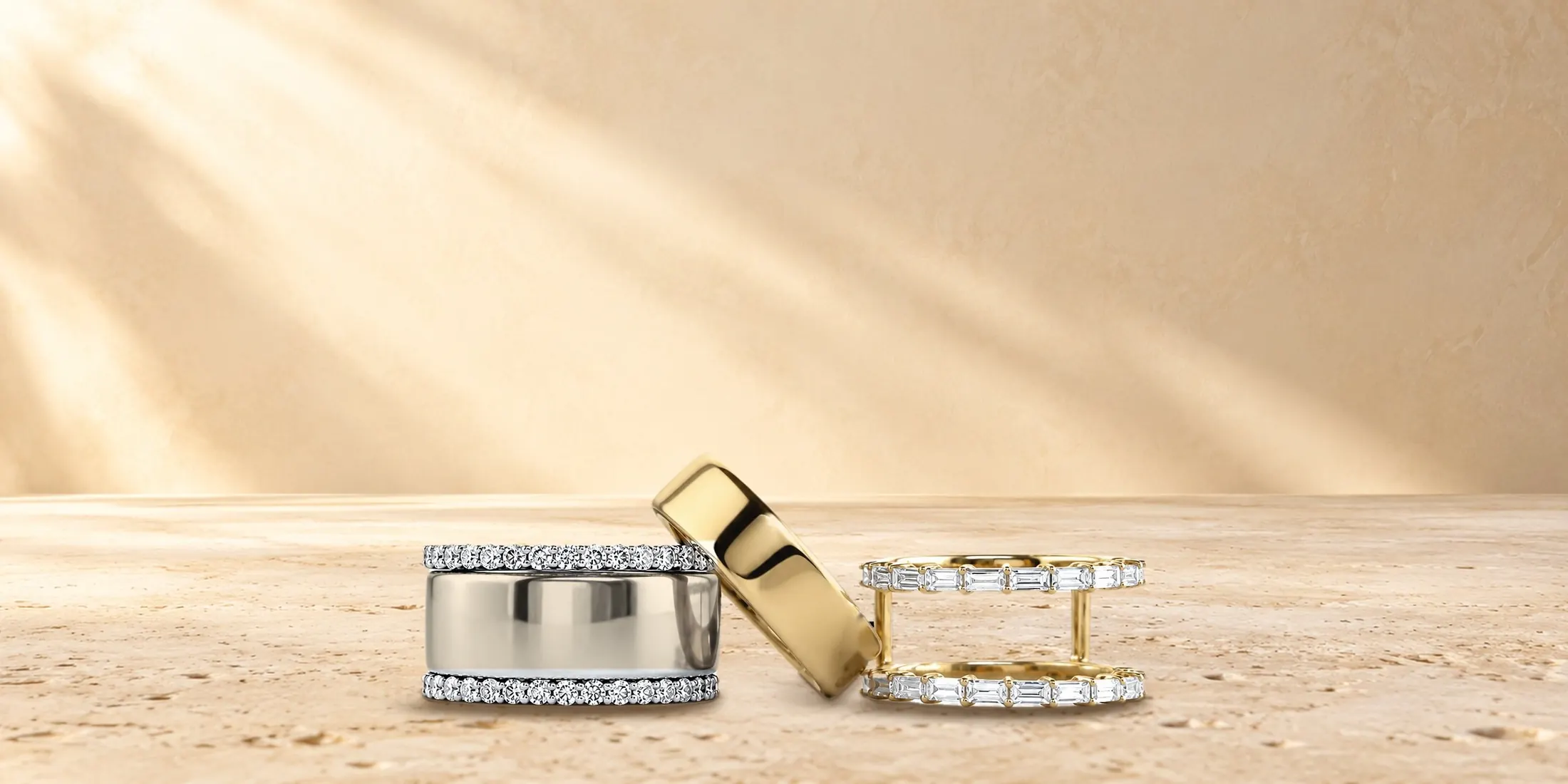 HALO Round in white gold, a gold Oura Ring and HALO Baguette in yellow gold on travertine