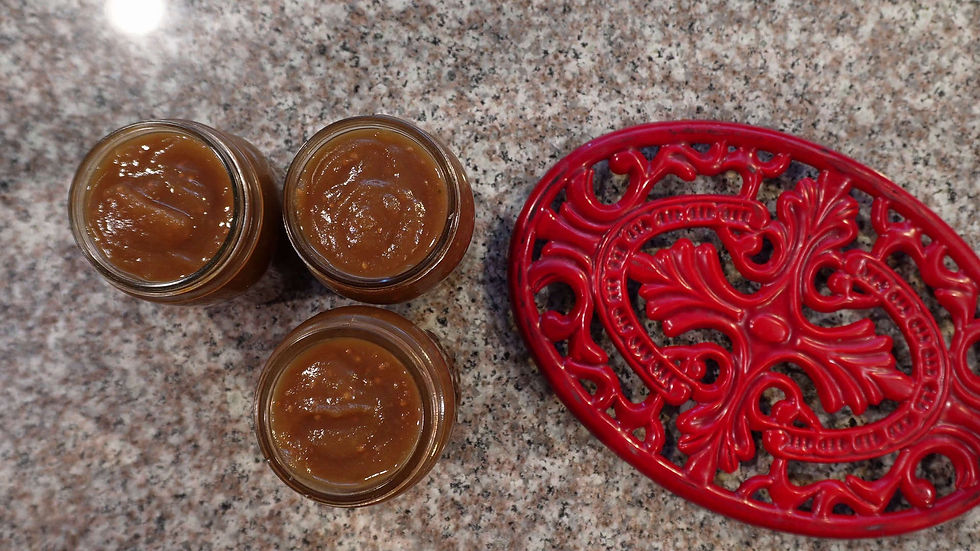 Three jars of brown jam on a speckled countertop. A red, ornate trivet is beside them, creating a cozy and vibrant kitchen scene.