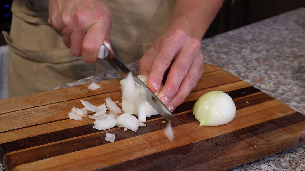 Hands slicing an onion on a wooden cutting board in a kitchen. The setting is cozy with a granite countertop, creating a homey mood.