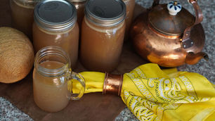 Jars of brown liquid with lids, a glass mug, a copper kettle, yellow patterned cloth, and brown twine on a speckled countertop.