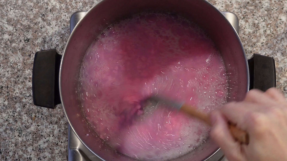 A person stirs pink liquid in a pot on a granite countertop. Bubbles form as the liquid swirls, creating a calming, dynamic motion.