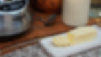 Butter slices on a white tray, with a Cuisinart food processor and a jar in the background, set on a wooden table with a striped mat.