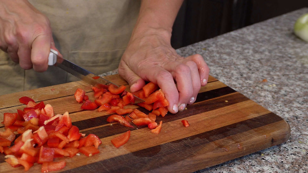 Hands chopping red bell pepper on a wooden cutting board. The background shows a granite countertop. Focused preparation scene.