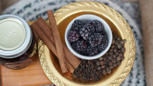 Frozen blackberries, cinnamon sticks, and spices on a gold tray beside a jar, in a cozy still life.