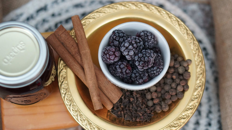 Frozen blackberries, cinnamon sticks, and spices on a gold tray beside a jar, in a cozy still life.