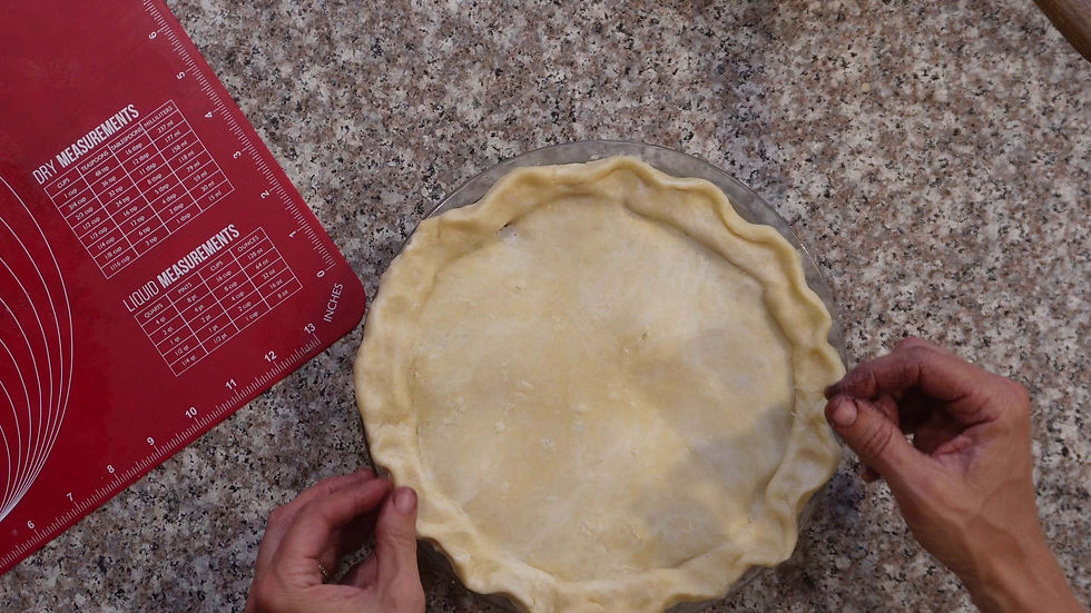 Hands crimp pie crust in a pie dish on a speckled countertop. A red mat with measurements is visible on the side.