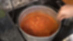 Pot of tomato soup being stirred on a stovetop. Hexagonal tile backsplash and granite countertop in the background.